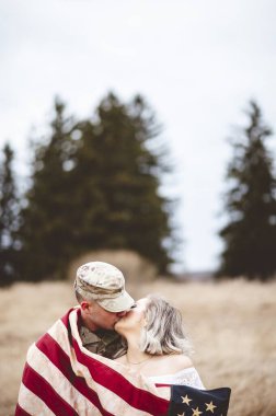 A shallow focus vertical shot of an American soldier kissing his loving wife while wrapped in an American flag clipart