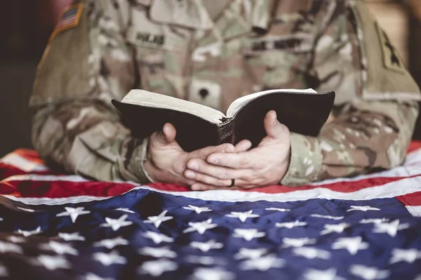 An American soldier mourning and praying with the Bible in his hands and the American flag