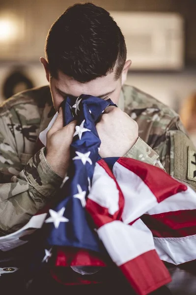 A vertical shot of an American soldier mourning and praying with the American flag in his hands