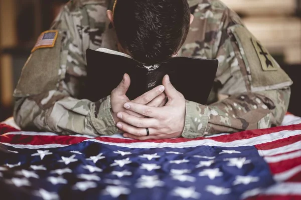 An American soldier mourning and praying with the Bible and the American flag in his hands