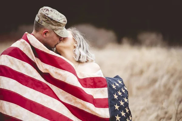 A shallow focus shot of an American soldier kissing his loving wife while wrapped in an American flag