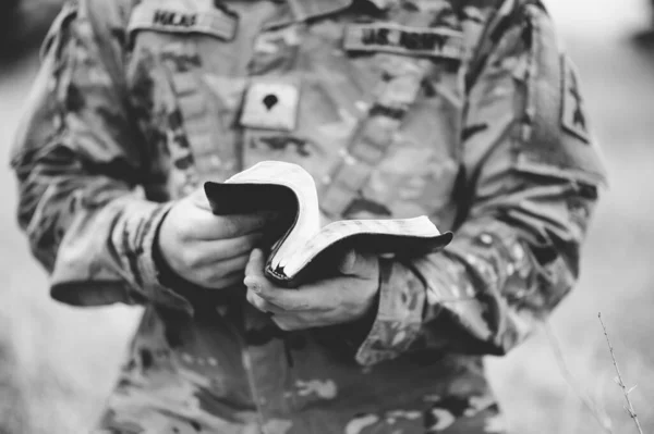一个年轻士兵在田野里拿着一本打开的圣经的灰度照片 — 图库照片