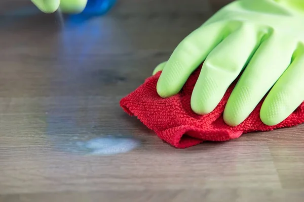 一个戴着橡胶手套的女佣用微型纤维清洁布和消毒喷雾器擦拭桌子 — 图库照片