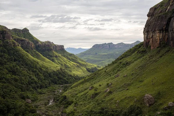 曇った灰色の暗い空の下で高い岩や急な丘と緑の谷の美しいショット — ストック写真
