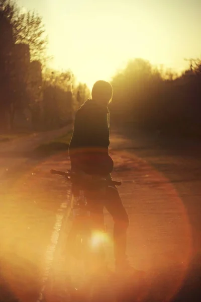 夕阳西下 一个人的轮廓靠在路上的一辆自行车上 — 图库照片