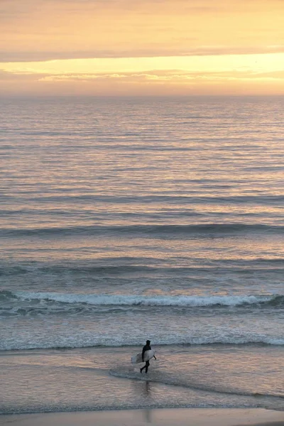 落日时与冲浪板一起在海滩上行走的人的垂直照片 — 图库照片
