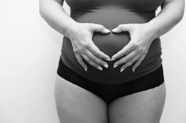 子宮に手を置いて心臓の形を作る妊婦の灰色のショット — ストック写真