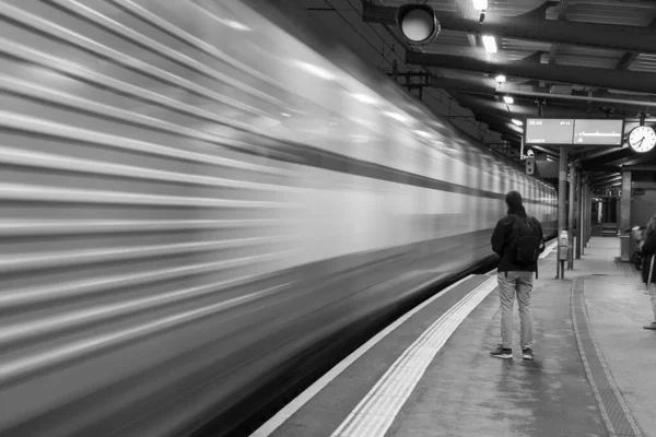 一个人在车站等火车 左边是一列模糊的火车 这是一张灰度的照片 — 图库照片