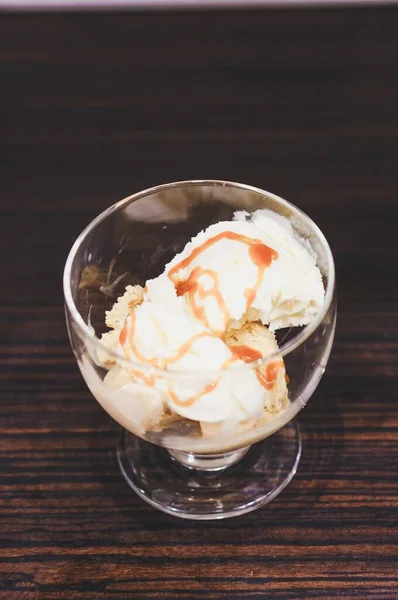 木製のテーブルの上にガラスカップにキャラメルシロップがトッピングされたアイスクリームのトップビュー — ストック写真