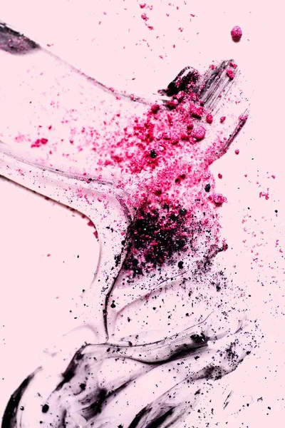 A vertical shot of pink and black powder with glitter smudged on a pink surface