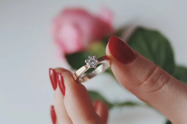 ピンクのバラを背景に金のダイヤモンドリングを持つ女性のクローズアップショット — ストック写真