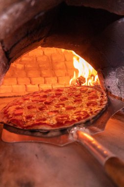 A vertical shot of a delicious cheesy pepperoni pizza inside the brick stone oven clipart