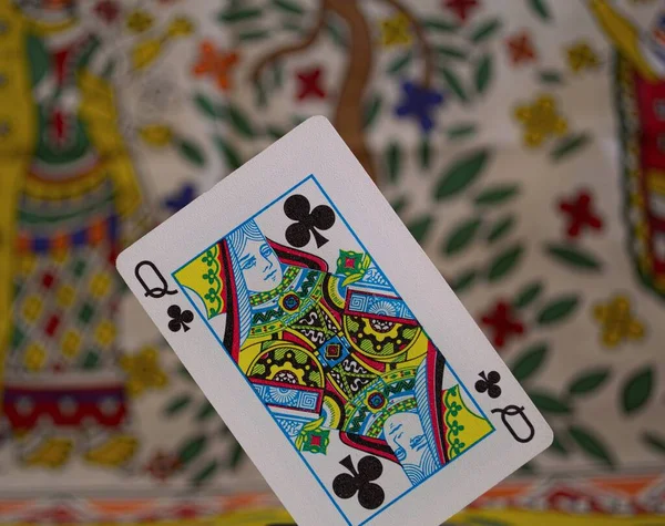 A closeup of a club queen card under the lights against a colorful blurry background