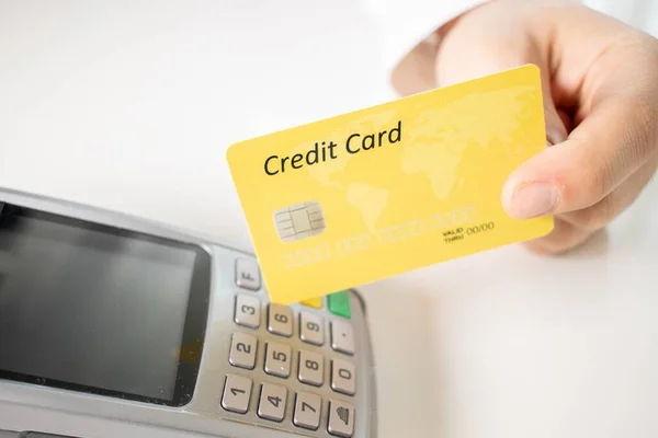 Zbliżenie Osoby Trzymającej Żółtą Kartę Kredytową Terminalem Płatniczym Białym Stole — Zdjęcie stockowe