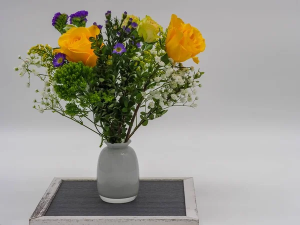 A picture of multicolor flowers in a white vase on a silver vintage chair against a grey background