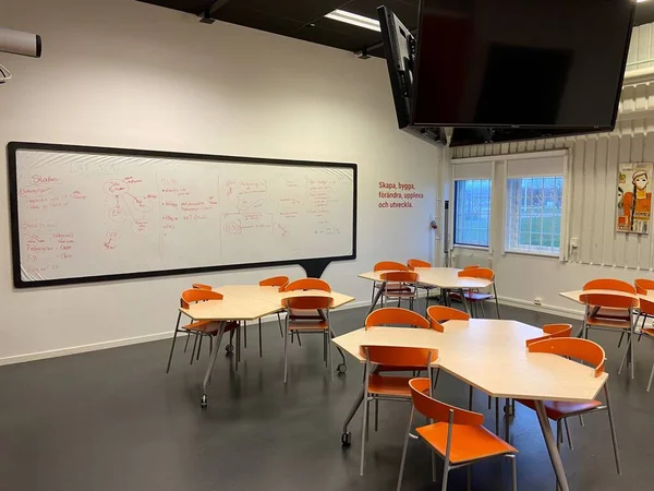 The interior of a modern classroom with geometric tables and orange chairs
