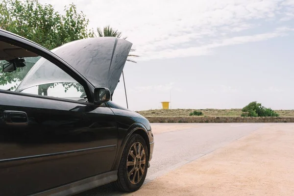 A black car with its hood open in the side of the road