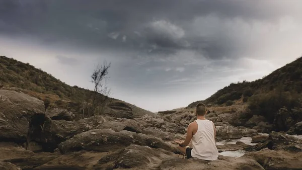 傍晚时分 一个人在多云的天空下 在被河流环绕的岩石上沉思 — 图库照片