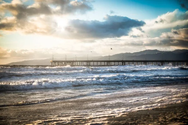 朝の曇り空の下 山に囲まれた桟橋のある波状の海の風景 — ストック写真