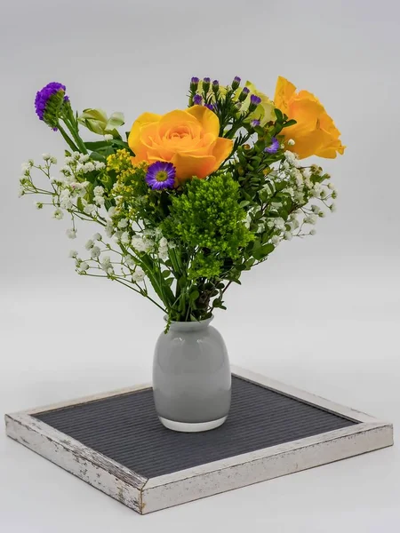 A vertical picture of multicolor flowers in a  vase on a silver vintage tray against a grey background