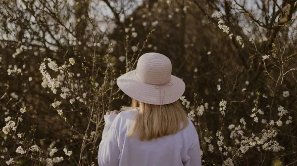 白い花の木の近くに帽子をかぶった女性 — ストック写真