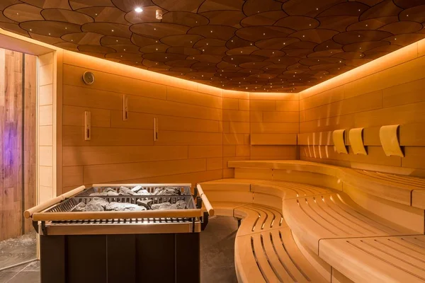 A beautiful sauna room design with a wooden bench and sauna rocks in the center