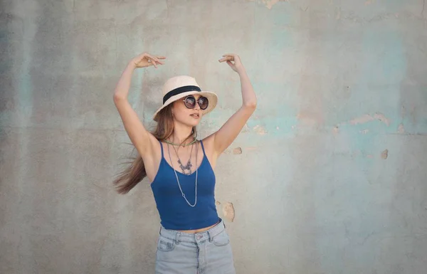 白い壁を背景に帽子や眼鏡などのアクセサリーを身に着けている青い袖の女性の美しいショット — ストック写真