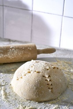 A closeup of a scoured dough sprinkled with flour and a rolling pin on the side clipart