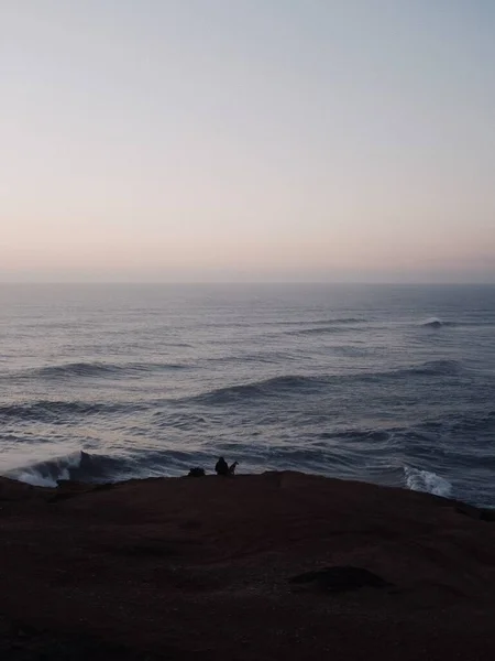 Вертикальний Знімок Людини Собакою Який Спостерігає Заходом Сонця Сидячи Пляжі — стокове фото