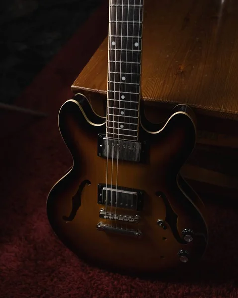 A vertical shot of a brown acoustic guitar on the ground