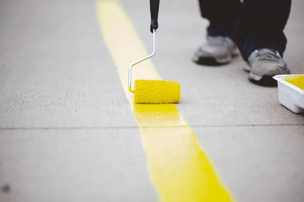 Ένας Άνθρωπος Ζωγραφίζει Μια Κίτρινη Γραμμή Τσιμεντένιο Έδαφος Χρησιμοποιώντας Έναν — Φωτογραφία Αρχείου