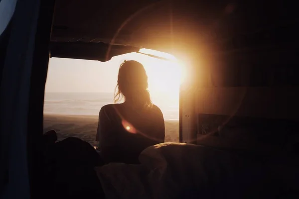 ビーチでキャンパーバンから夕日を見ている大人の女性の魅惑的な景色 — ストック写真