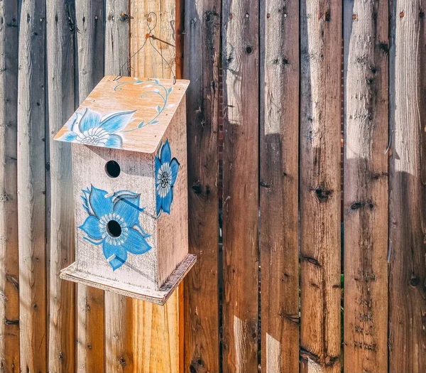 木製の柵に吊るされた鳥の家に描かれた青い花のクローズアップ — ストック写真