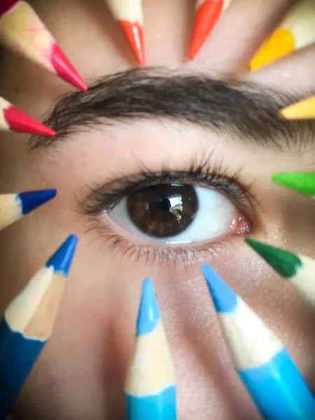 カラフルな鉛筆で囲まれた子供の目の垂直ショット — ストック写真