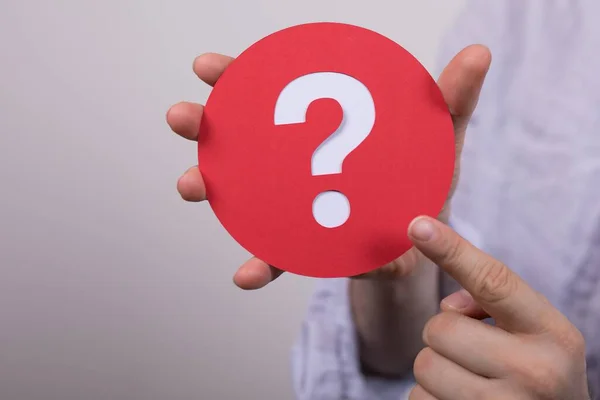 A sign of the question mark made of red paper in the hands of a man