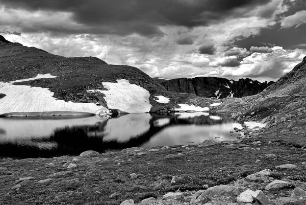 Серый Снимок Озера Окруженного Высокими Скалистыми Заснеженными Горами Облачным Небом — стоковое фото