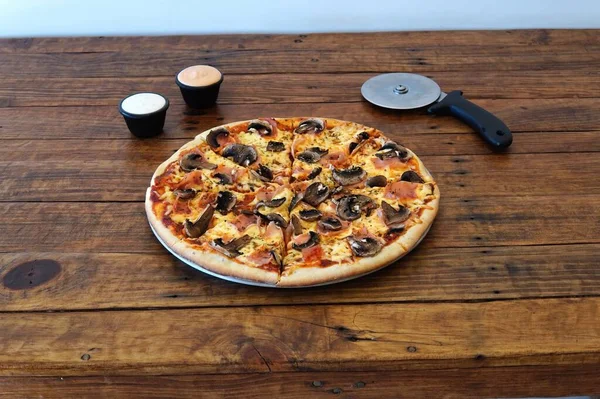 A closeup shot of a pizza with sauces and a cutter on a wooden table