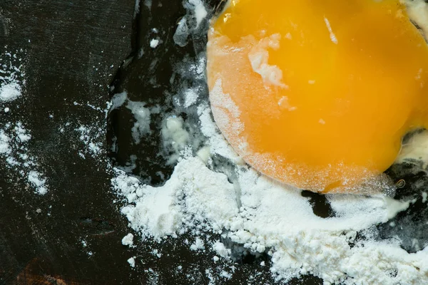 Wheat flour and a broken yellow egg on a black kitchen table — Stock Photo, Image