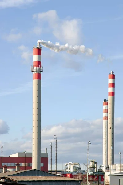 Industrial chimney emitting white smoke. Pollution from chemical industry. Group of factory chimneys with red / white stripes. Blue background, industrial landscape.