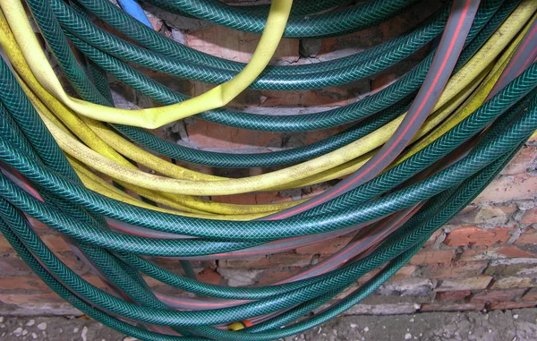 Multicolored watering hoses are suspended against a red brick wall. Hoses unevenly SAG and get mixed up among themselves. Some crumpled, some filled. close-up shooting.