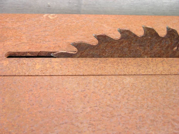 Büyük bir ahşap işçiliği makinesinin paslı kırmızı yüzeyleri. Çerçevedeki küçük bir delikten çıkan büyük bir anti-diluvian kesicisi korozyon tarafından ele geçirilmiş. Kesici dişler tarih öncesi zamanlarda omurga boyunca bir dinozorun tepesine benzer..