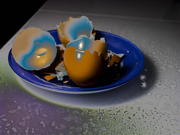 Abstraction on a theme broken eggshell on a saucer of unbreakable glass. Around on the glossy surface of a water drop. Close-up, narrow focus. 