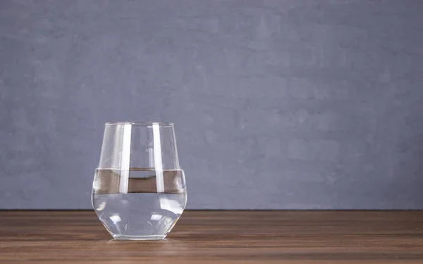 empty water glass, on wooden floor, in front of concrete floor