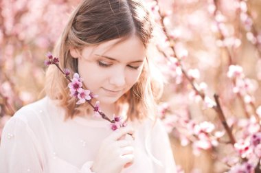 Smiling blonde girl holding peach flowers outdoors closeup. Spring season. 