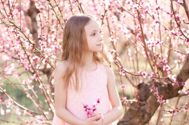 Baby girl 4-5 year old posing peach flowers outdoors. Looking away. Spring season. 