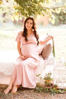 Smiling pregnant woman sitting in bed outdoors over nature background. Looking at camera. Motherhood. 