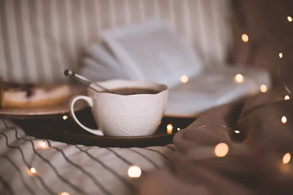 背景に輝くライトの上にベッドの中で開いて本を持つ新鮮な紅茶のカップ おはようございます朝食の時間 — ストック写真