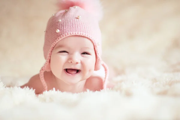 ニットのピンクの帽子をかぶった1歳以下の赤ちゃんがベッドの上に横たわって笑っています カメラを見て幸せよ幼少期 — ストック写真