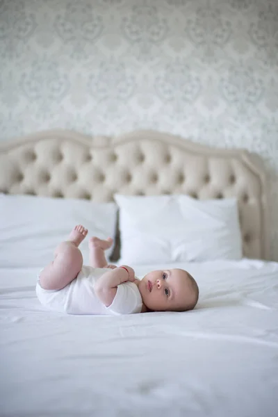 1歳未満のかわいい赤ちゃんは ベッドルームのクローズアップでベッドに横たわって白いボディスーツを着ています 子供の頃おはようございます — ストック写真