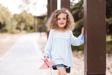 4-5 yaşlarında şık bir kız çocuğu, elinde origami vinçle parkta poz veriyor. Kameraya bakıyorum. Çocukluk. 